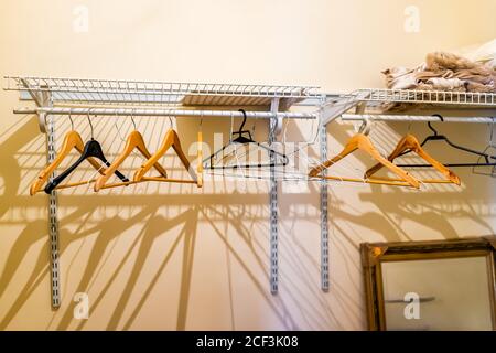 Many empty closet hangers in room on rack stand in hotel or house with yellow light and shadows with nobody home interior and mirror Stock Photo