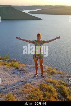 Happy girl agaist beautiful fiord. Woman dressed in bright summer dress. Evening time. Summer. Stock Photo
