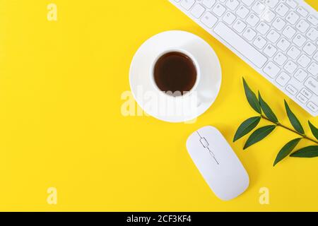 Office workplace with keyboard, computer mouse, cup of coffee and plant on yellow background. Flat lay, top view Stock Photo