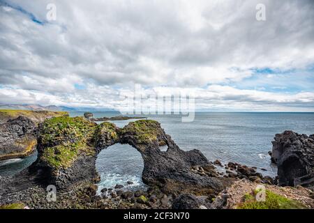 Landscape view of Gatklettur arch famous rock near Hellnar, National park Snaefellsnes Peninsula, Iceland with rocky ocean sea waves green grass moss Stock Photo