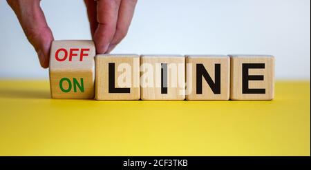 Hand turns a cube and changes the word 'offline' to 'online' or vice versa. Beautiful yellow table, white background. Business concept. Copy space. Stock Photo