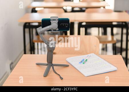 Phone gimbal stabilizer with a phone on a desk in an empty classroom, new normal back to school during Covid-19 Stock Photo
