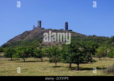 Ruines of hazmburk castle on top of mountain peak of ceske stredohori range. Fruit trees and blue sky. Stock Photo
