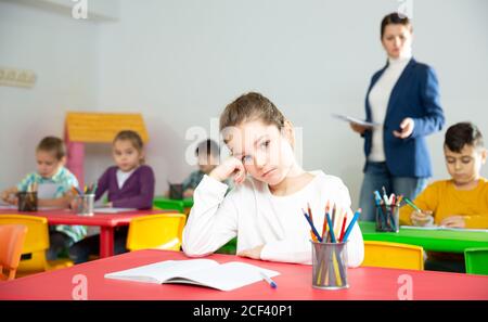 Portrait of tired schoolgirl sitting at pupils desk at lesson in primary school Stock Photo