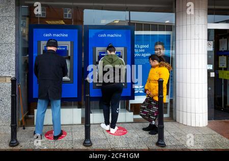 A man and a woman side by side withdrawing cash from a Halifax Bank  ATM or Cash Machine while a girl looks on Stock Photo