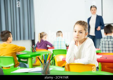 Sad bored schoolgirl sitting separately in classroom during lesson in elementary school Stock Photo