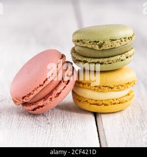 Colorful tasty macaroons stacked in pile against wooden white surface Stock Photo