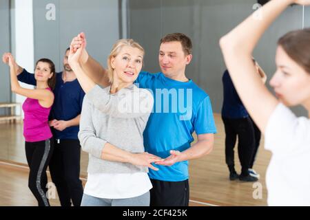 Smiling middle aged woman practicing bachata movements in dance studio for adults Stock Photo