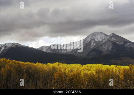 Storm clouds gathering around the snow covered peaks of the La Sal Mountains of Utah, USA, with Aspen in golden fall colors lit by the last sunlight Stock Photo