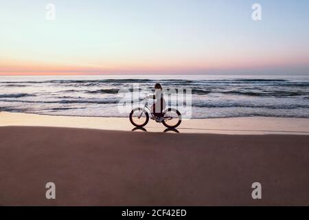 Joyful Woman riding bicycle along peaceful beach Stock Photo