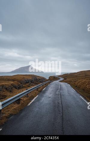 Curvy asphalt road going through hilly terrain on cloudy day on Faroe Islands