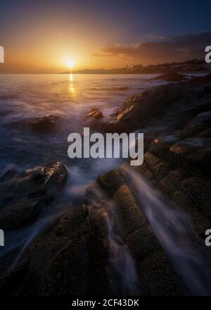 Picturesque view of clean sea water rolling and splashing near rough stones during wonderful sundown Stock Photo