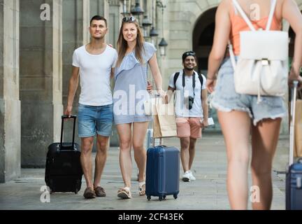Positive family tourists taking promenade and dragging suitcases in city on vacations Stock Photo