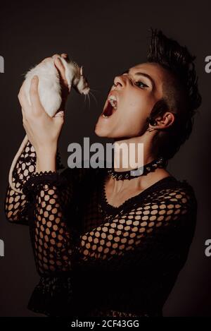 Confident Woman with mohawk carrying white rat on shoulder and looking at camera against black background Stock Photo