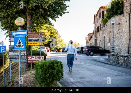 Castiglione del Lago, Italy - August 28, 2018: Umbria sunny summer day with street road and person walking by direction signs exterior of fortress cit Stock Photo