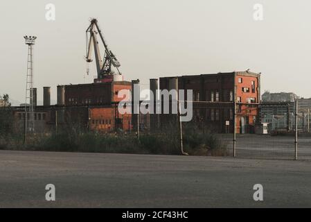 Old functioning red brick factory buildings, pipes and crane placing on industrial area behind fence Stock Photo
