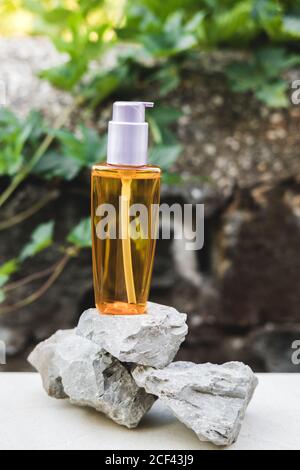 An orange oil bottle next to natural stones against a gray wall with natural light. Trendy style. Cosmetic mockup. Copyspace Stock Photo