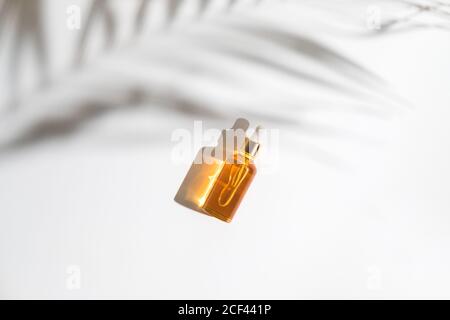 White, orange and black serum bottles on white background. Trending shadow from a palm branch. Cosmetic mockup. Place to insert text, images. Top view Stock Photo
