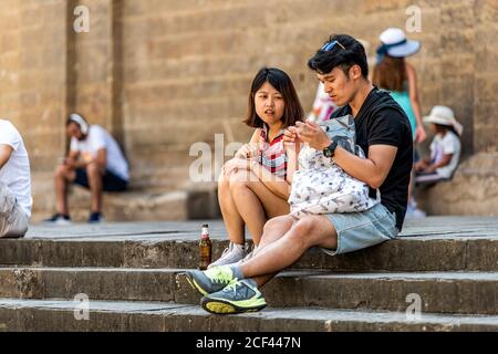 Firenze, Italy - August 30, 2018: Couple tourists young asian people sitting resting on street square outside in summer day in Florence, Tuscany Stock Photo