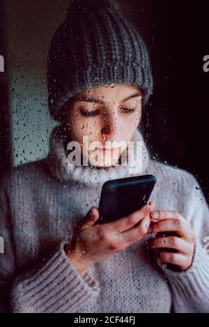 Young Woman with smartphone standing near window Stock Photo