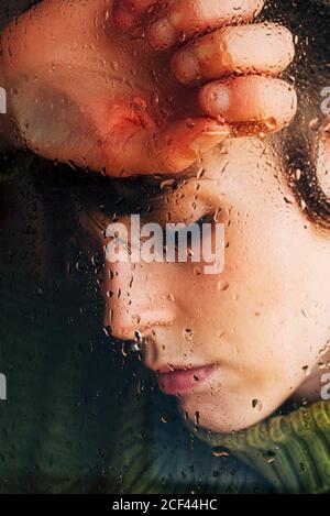 Melancholic young Woman looking through window Stock Photo
