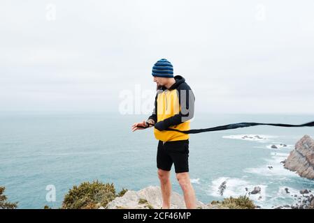 Bearded adult man wrapping bandage around hand while standing against sea during outdoor kickboxing training Stock Photo