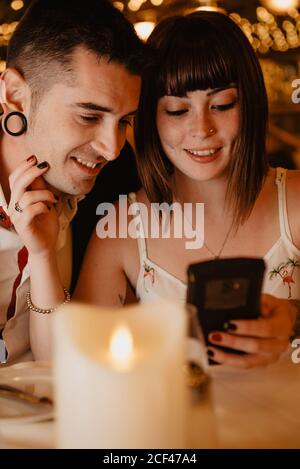 Young man and Woman smiling and browsing modern smartphone together while sitting at table during romantic dinner in luxury restaurant Stock Photo