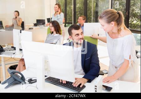 Young business woman explaining something to male colleague at computer monitor Stock Photo
