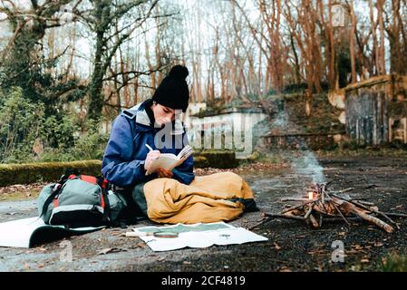 Young female backpacker making notes at campfire Stock Photo