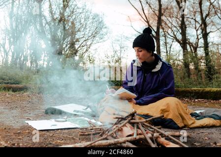 Young female backpacker making notes at campfire Stock Photo