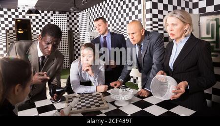 Group of businesspeople standing together near chessboard in quest room solving conundrum. Business teamwork concept Stock Photo