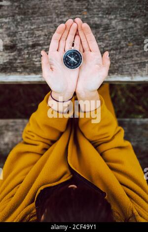 From above anonymous female holding small vintage compass in hands over wooden table during trip in countryside Stock Photo