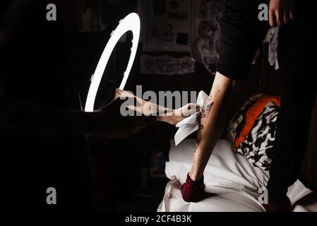 unrecognizable man tattooer using smartphone to take picture of tattoo on leg of crop customer for portfolio in contemporary studio Stock Photo
