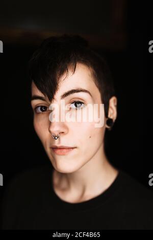 Modern trendy female with short hair and piercing in nose looking at camera against black background Stock Photo