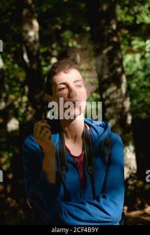 Calm young female tourist resting and smoking marijuana joint while hiking in forest in summer Stock Photo