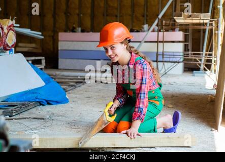 girl working with wood in workshop. carpentry and woodwork concept. Portrait of a cute kid posing as a carpenter, with a handsaw. working as woodworker. carpenter in protective hat work. Stock Photo