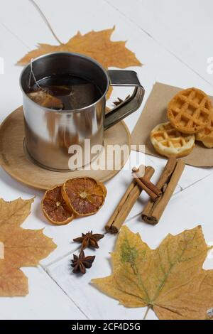 Mug of tea and waffles. Nearby are dried maple leaves, cinnamon, anise and dried oranges on the table. Autumn still life. Stock Photo