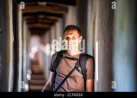 Young man looking at camera happy face portrait in light standing in fortress tunnel passage in Castiglione del Lago, Italy Stock Photo