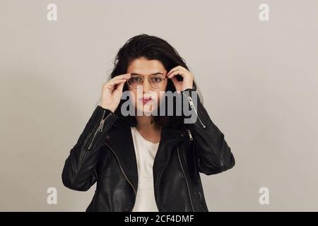 Thoughtful attractive dark haired Woman in black biker jacket and looking at camera on gray background in studio Stock Photo