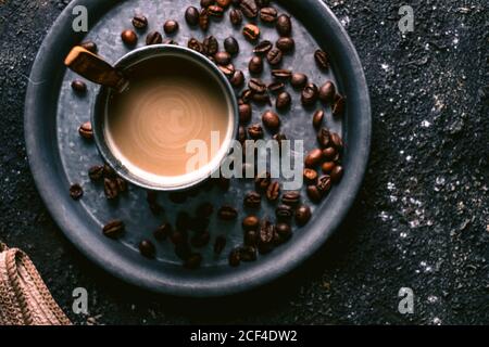 Top view of coffee grains and cup with fresh coffee and spoon placed on metal tray on rough table Stock Photo