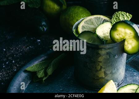 From above metal mug of cold cucumber detox drink with slices of lime and leaves of mint placed on tray Stock Photo