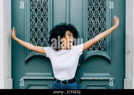 Young African American Woman standing with closed eyes by green wooden door and sticking out tongue on daytime Stock Photo