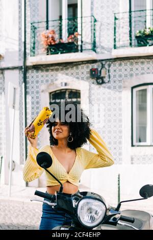 Young African American Woman with black curly hair sitting on motorcycle and closed eyes with bag on hand Stock Photo