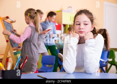 Sad bored schoolgirl sitting separately in classroom in break between lessons Stock Photo