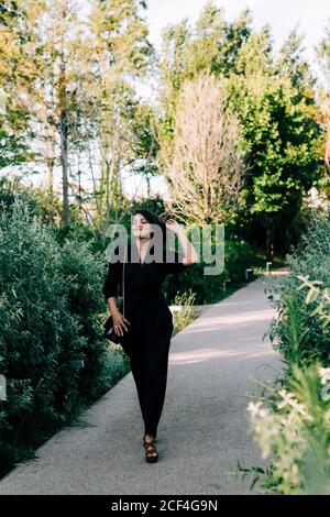 Trendy young Woman in black suit walking along paved path and enjoying summer day in Lisbon Stock Photo