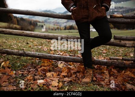 Cropped unrecognizable man leaning at a wooden fence in a beautiful rural mountain landscape in autumn in Dolomites, Italy Stock Photo