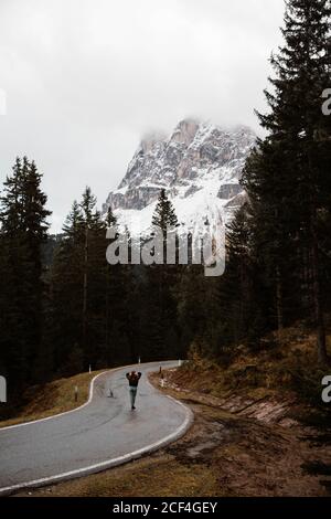 Tourist person on empty route amid big pine forest standing and enjoying in views of powerful Dolomites mountains at Italy Stock Photo