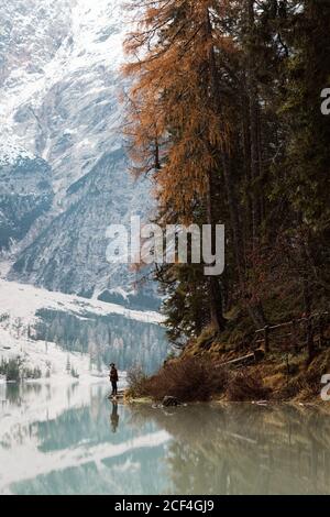 Back view of anonymous man traveler in casual wear standing and delighting in view of turquoise lake with foggy Dolomites mountains on background at Italy Stock Photo