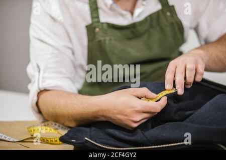 unrecognizable male seamstress using measuring tape while checking exact size of patterns while making bespoke outfit for client in modern atelier Stock Photo