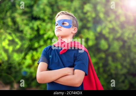 Superhero kid boy against green background outdoor. Childhood, success and and power concept Stock Photo